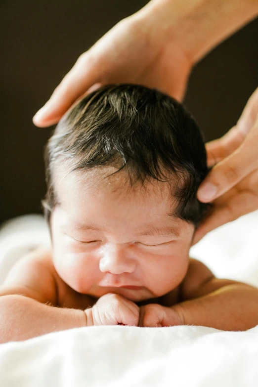 a close up of a baby laying on a bed, by Elizabeth Durack, unsplash, renaissance, greeting hand on head, acupuncture treatment, japanese, hair