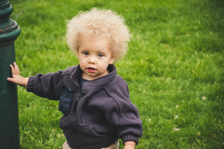 a little boy standing next to a green pole, by Sophia Beale, pexels contest winner, short blonde afro, walking on grass, toddler, caring fatherly wide forehead