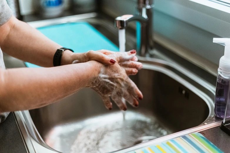 a woman washing her hands in a kitchen sink, by Julia Pishtar, pexels contest winner, fan favorite, healthcare worker, bumpy skin, stainless steel