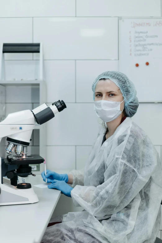 a woman in a lab coat sitting in front of a microscope, a microscopic photo, surgical gown and scrubs on, in a research facility, trending photo, thumbnail