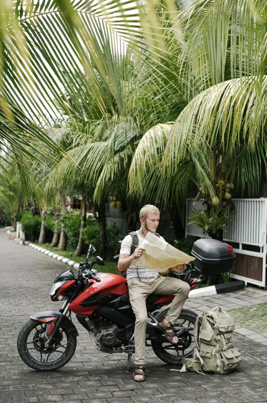 a man riding on the back of a red motorcycle, by Daren Bader, tropical palms, reading a newspaper, bali, a blond