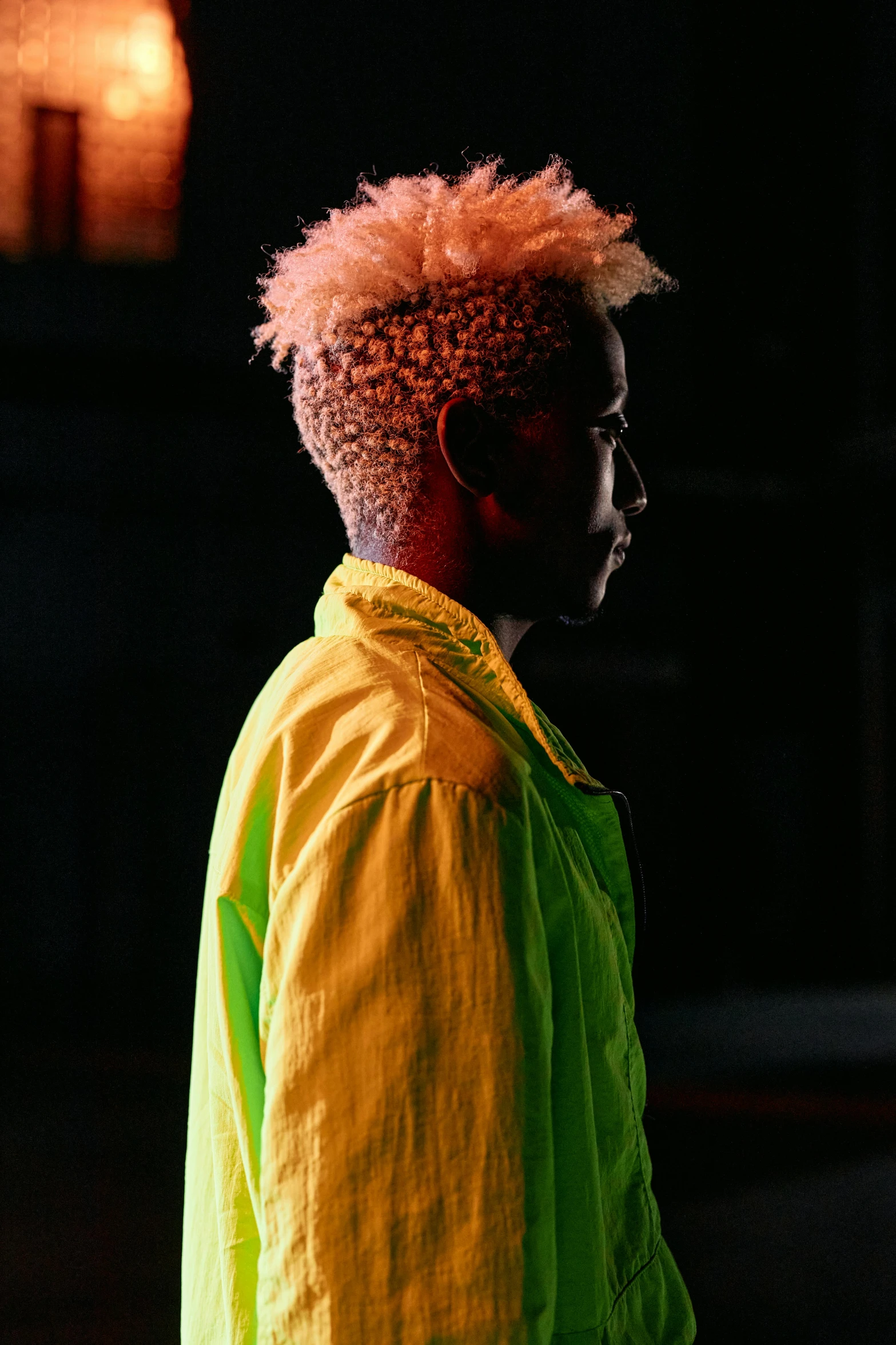 a man with pink hair standing in a dark room, inspired by Barthélemy Menn, trending on pexels, afrofuturism, yellow and green, short blonde afro, yellow clothes, profile shot