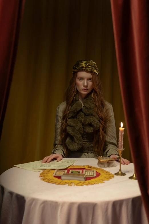 a woman sitting at a table with a candle, by Wes Anderson, renaissance, wearing a crown and cape, ignant, a redheaded young woman, photographed for reuters