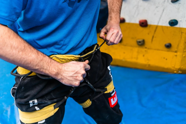 a man standing in front of a climbing wall, unsplash, figuration libre, black and yellow tracksuit, huge belt, high angle close up shot, martial arts tournament