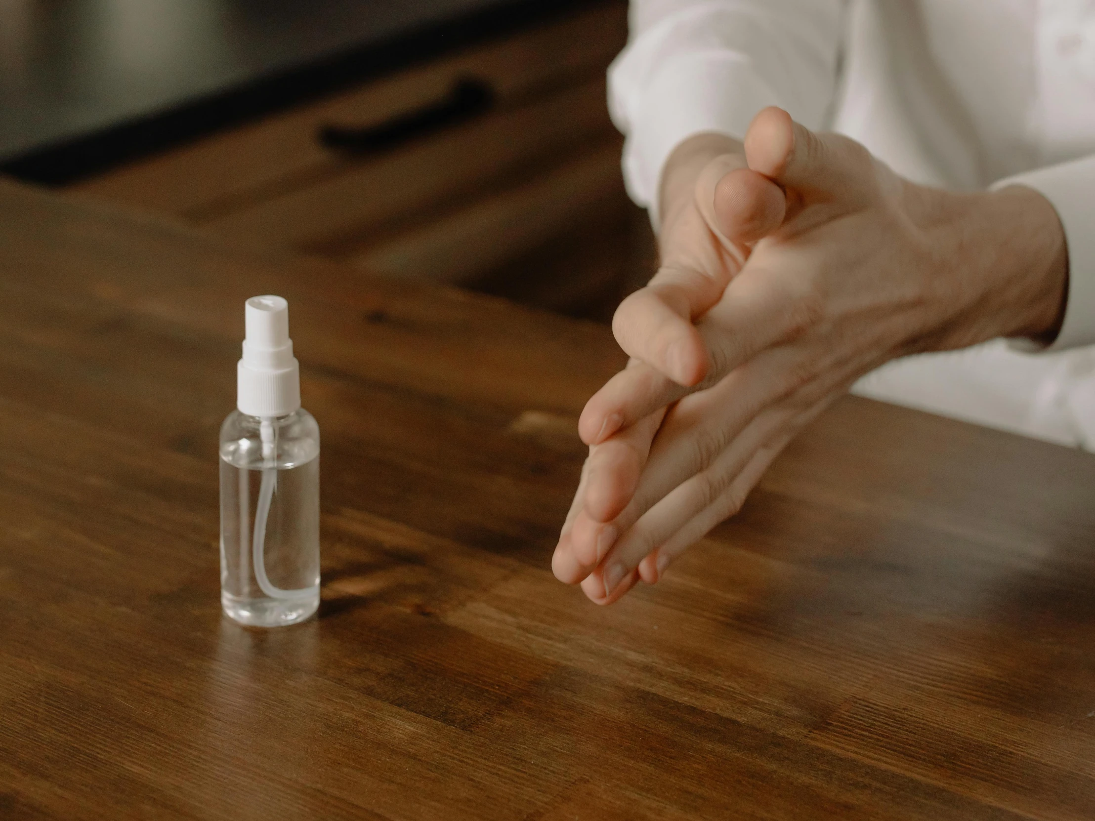 a person sitting at a table with a bottle of hand sanitizer, trending on pexels, hyperrealism, spinning hands and feet, a wooden, sprays, transparent
