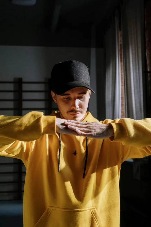 a man in a yellow hoodie poses for a picture, inspired by Chen Chi, trending on pexels, dancer, praying posture, baggy clothing and hat, avatar image