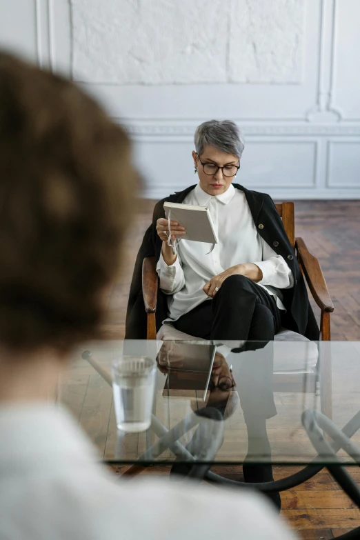 a woman sitting in a chair looking at a tablet, a portrait, pexels contest winner, realism, business meeting, androgynous person, white reading glasses, image split in half