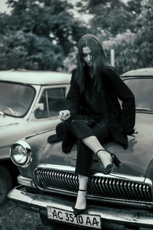 a woman sitting on the hood of a car, inspired by Peter Lindbergh, pexels contest winner, auto-destructive art, black loafers, goth chic, late 1 9 6 0's, handsome girl