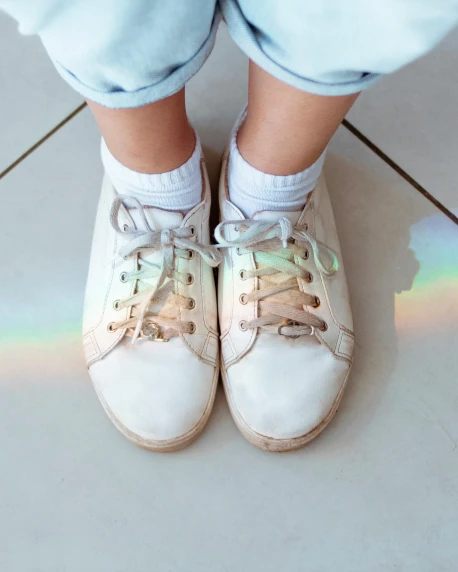 a close up of a person's shoes on a tiled floor, by Helen Stevenson, trending on unsplash, grey skies with two rainbows, wearing white clothes, 4yr old, prism lights