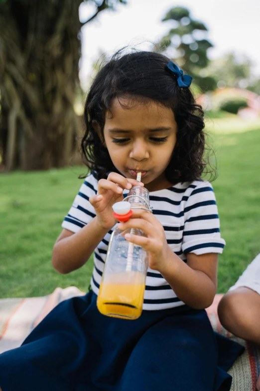 a couple of kids sitting on top of a blanket, pexels, ice tea in a mason jar, indian girl with brown skin, at a park, high resolution photo