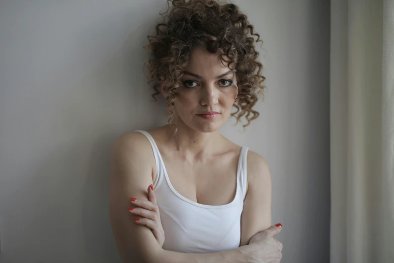 a woman leaning against a wall with her arms crossed, pexels contest winner, curly and short top hair, photo of džesika devic, human actress, annoyed