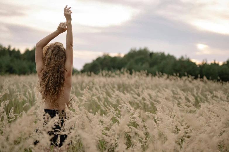 a woman standing in a field of tall grass, unsplash, naturalism, waving arms, furr covering her chest, biophilia, bare shoulders