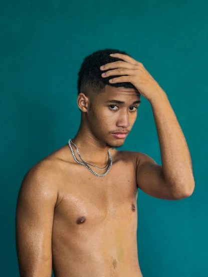 a shirtless young man standing in front of a blue wall, an album cover, trending on pexels, realism, rapper jewelry, 😭 🤧 💔, non binary model, mixed race