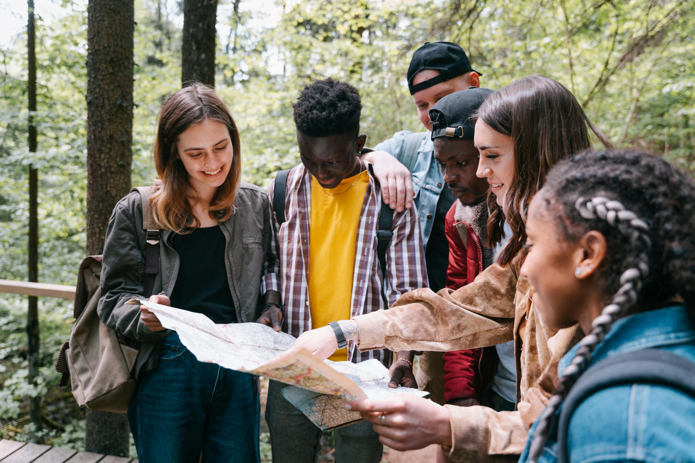 a group of people looking at a map in the woods, by Emma Andijewska, pexels contest winner, varying ethnicities, teenage girl, promotional image, college