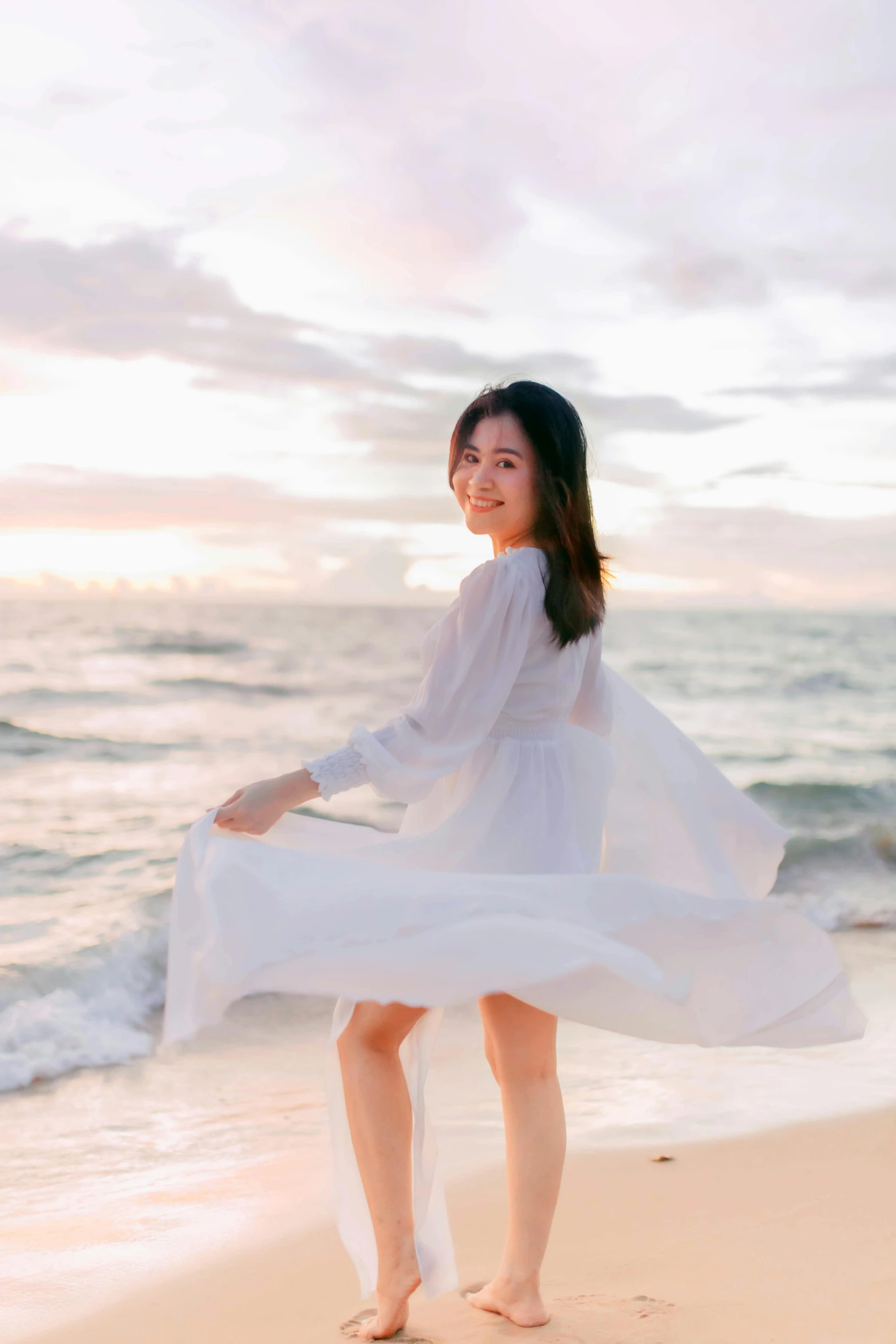 a woman standing on top of a beach next to the ocean, by Tan Ting-pho, romanticism, wearing a cute white dress, smiling playfully, wearing a long flowy fabric, 8 k )