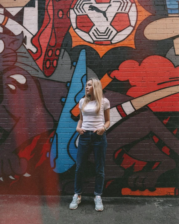 a woman standing in front of a graffiti wall, trending on unsplash, wearing pants and a t-shirt, lgbtq, sydney sweeney, background image