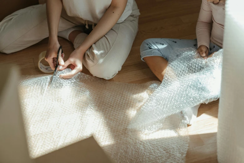 a woman sitting on the floor with a pair of scissors, trending on pexels, plasticien, plastic wrap, 2 people, weaving, made of cardboard