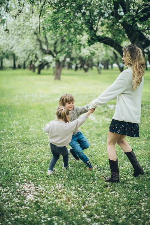 a woman and two children holding hands in a park, an album cover, pexels contest winner, playful pose, grassy field, blossoms, game