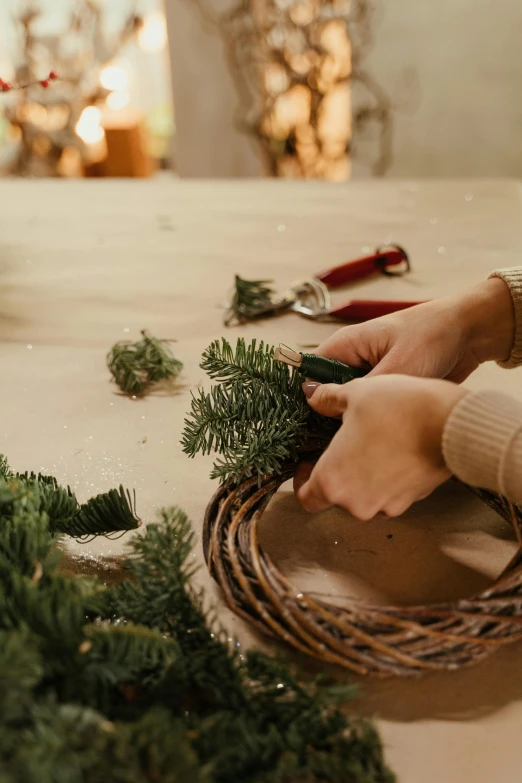 a person making a wreath on a table, inspired by Patrick Dougherty, trending on pexels, holiday season, low detail, cut, winter setting