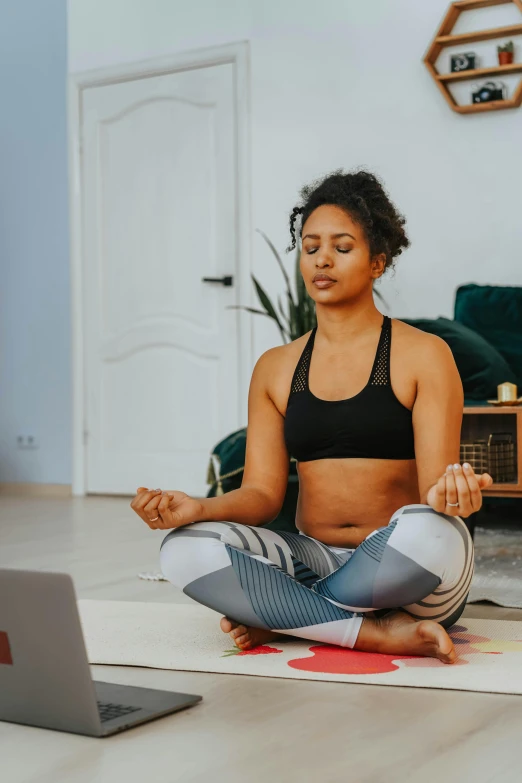 a woman sitting on a yoga mat in front of a laptop, trending on pexels, happening, praying meditating, african american woman, low quality photo, lotus pose