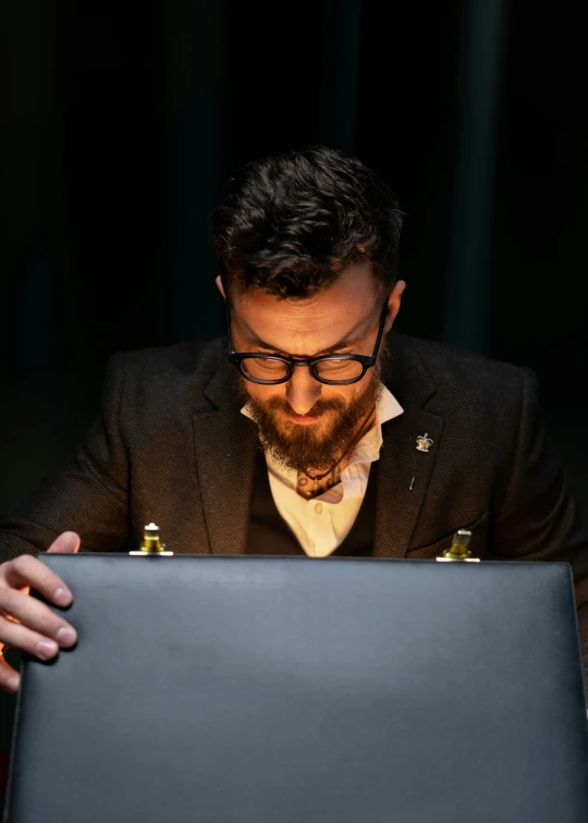 a man sitting in front of a laptop computer, by Jacob Toorenvliet, trending on reddit, holding grimoire, performance, neat beard, looking at the treasure box