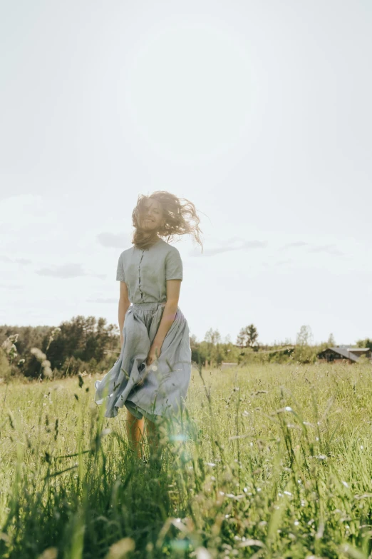 a woman standing in a field with her hair blowing in the wind, trending on unsplash, happening, sundress, grey, walking on grass, 15081959 21121991 01012000 4k