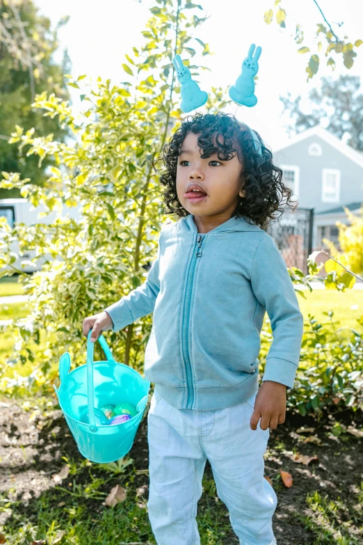 a little girl that is standing in the grass, wearing a blue hoodie, with an easter basket, seafoam green, hero shot