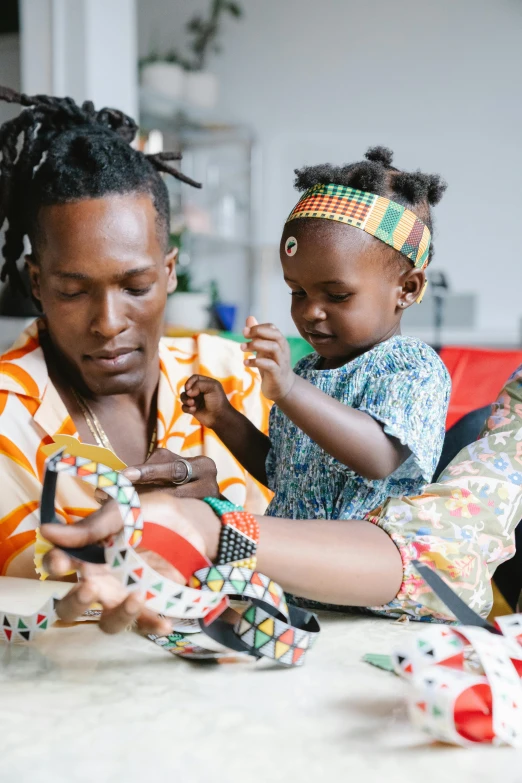 a woman and a child sitting on a couch, trending on unsplash, black arts movement, short dreadlocks with beads, art toys on feet, handsome man, patterned clothing