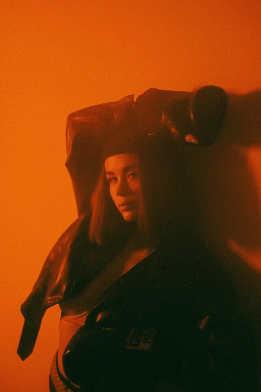 a woman that is standing in front of a wall, an album cover, inspired by Elsa Bleda, unsplash, renaissance, orange tint, wearing a dark hood, charli xcx, concert