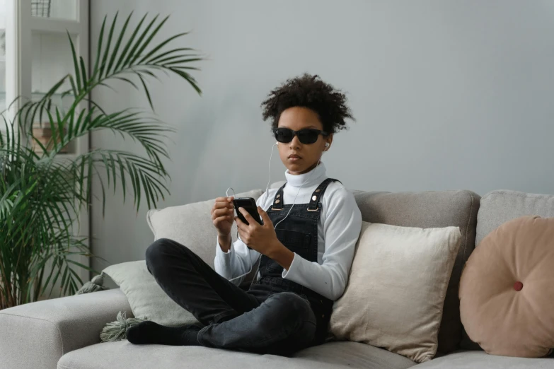 a woman sitting on a couch using a cell phone, by Adam Marczyński, trending on pexels, afrofuturism, television sunglasses, black teenage boy, slight overcast, gamer aesthetic