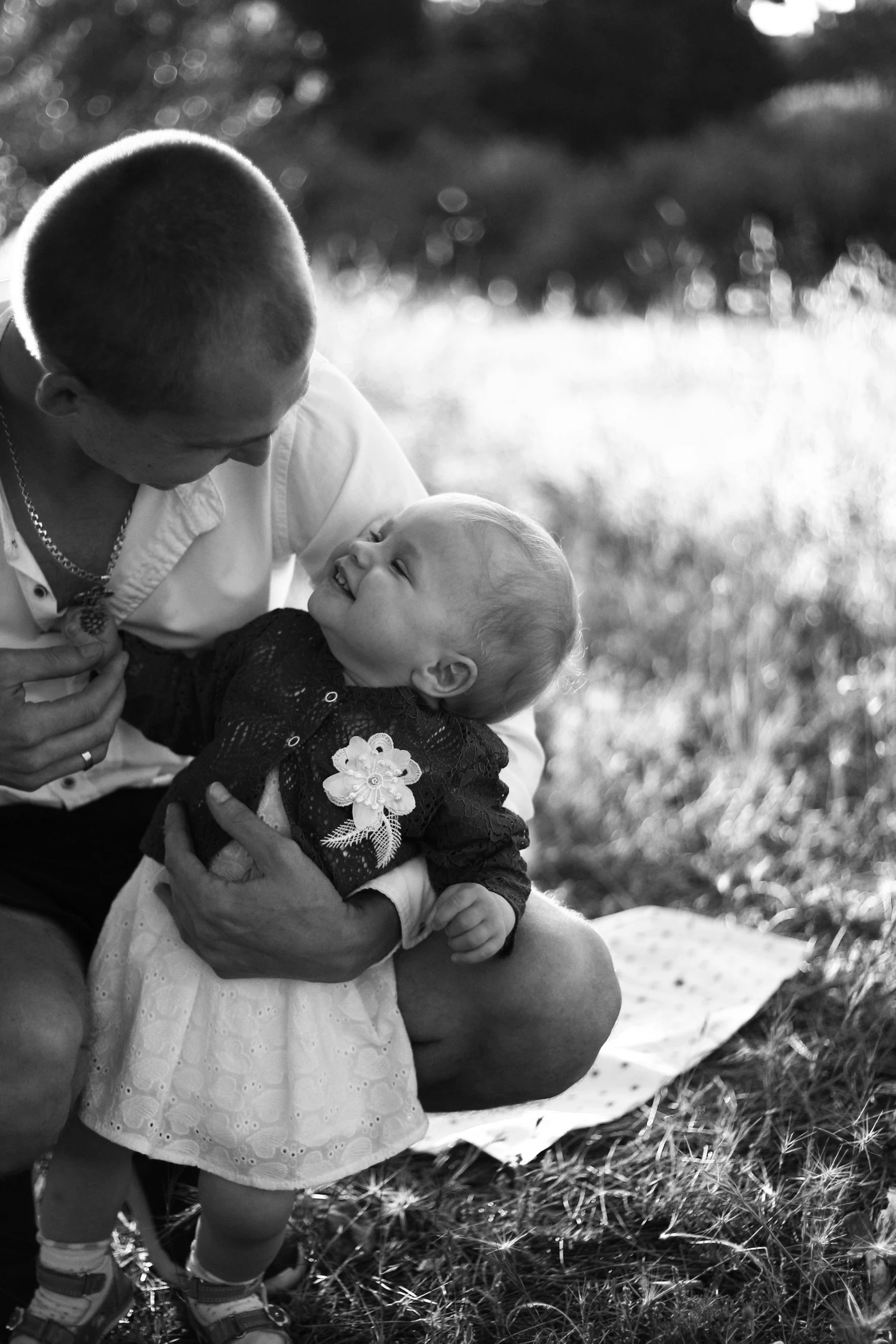 a black and white photo of a man holding a baby, a black and white photo, by Felix-Kelly, sparkling in the sunlight, (beautiful) girl, high quality upload, looking at the ground