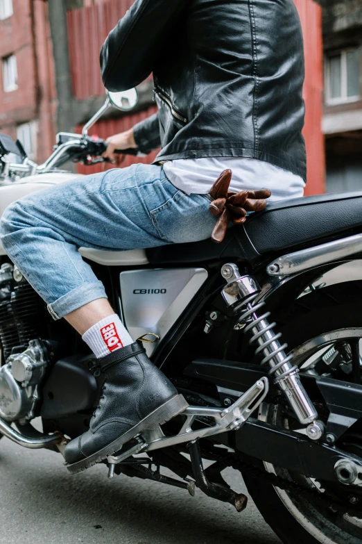 a man riding on the back of a motorcycle down a street, by Nina Hamnett, trending on unsplash, jeans and boots, with white kanji insignias, model posing, leather cuffs around wrists