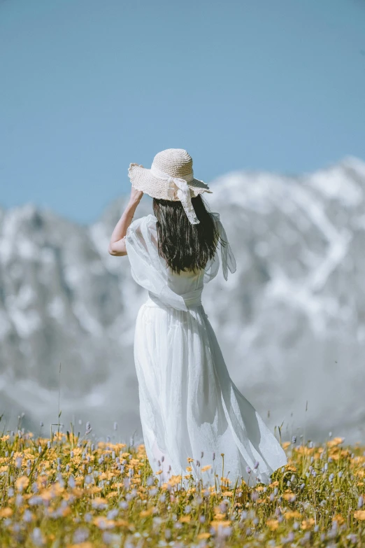 a woman in a white dress and hat standing in a field of flowers, pexels contest winner, in the snow mountains, award winning fashion photo, chiffon, back