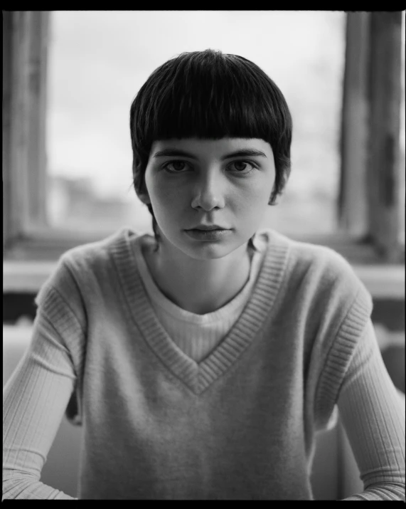 a black and white photo of a woman sitting at a table, a black and white photo, inspired by Antanas Sutkus, with short hair with bangs, very very very pale skin, attractive girl tomboy, david kassan