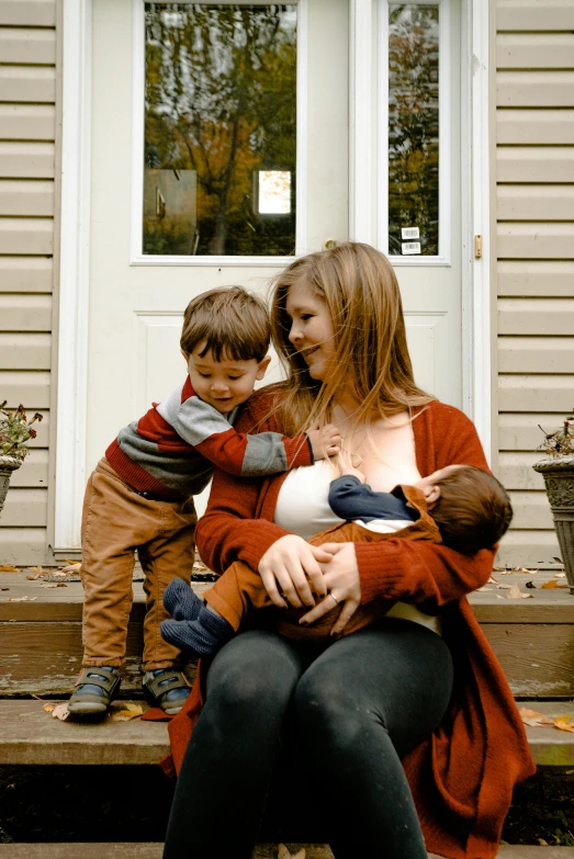 a woman sitting on a porch holding a baby, pexels, milk duds, boys, fall season, avatar image