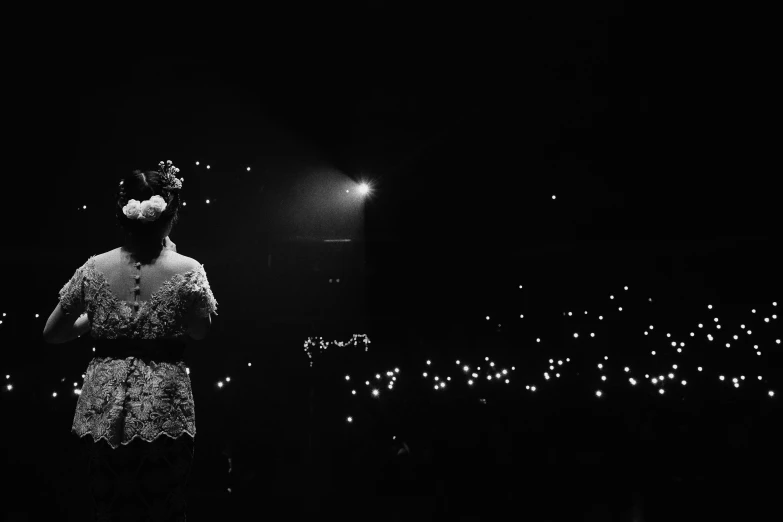 a woman that is standing in the dark, a black and white photo, unsplash, happening, live concert, melanie martinez, shot on iphone 6, intricate sparkling atmosphere