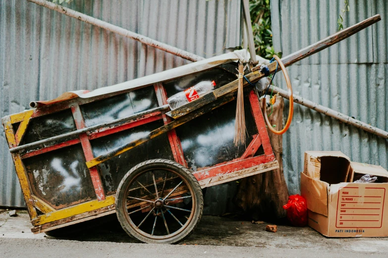 a red and yellow cart sitting on the side of a road, pexels contest winner, mingei, scrap metal on workbenches, dingy, background image, an unknown ethnographic object