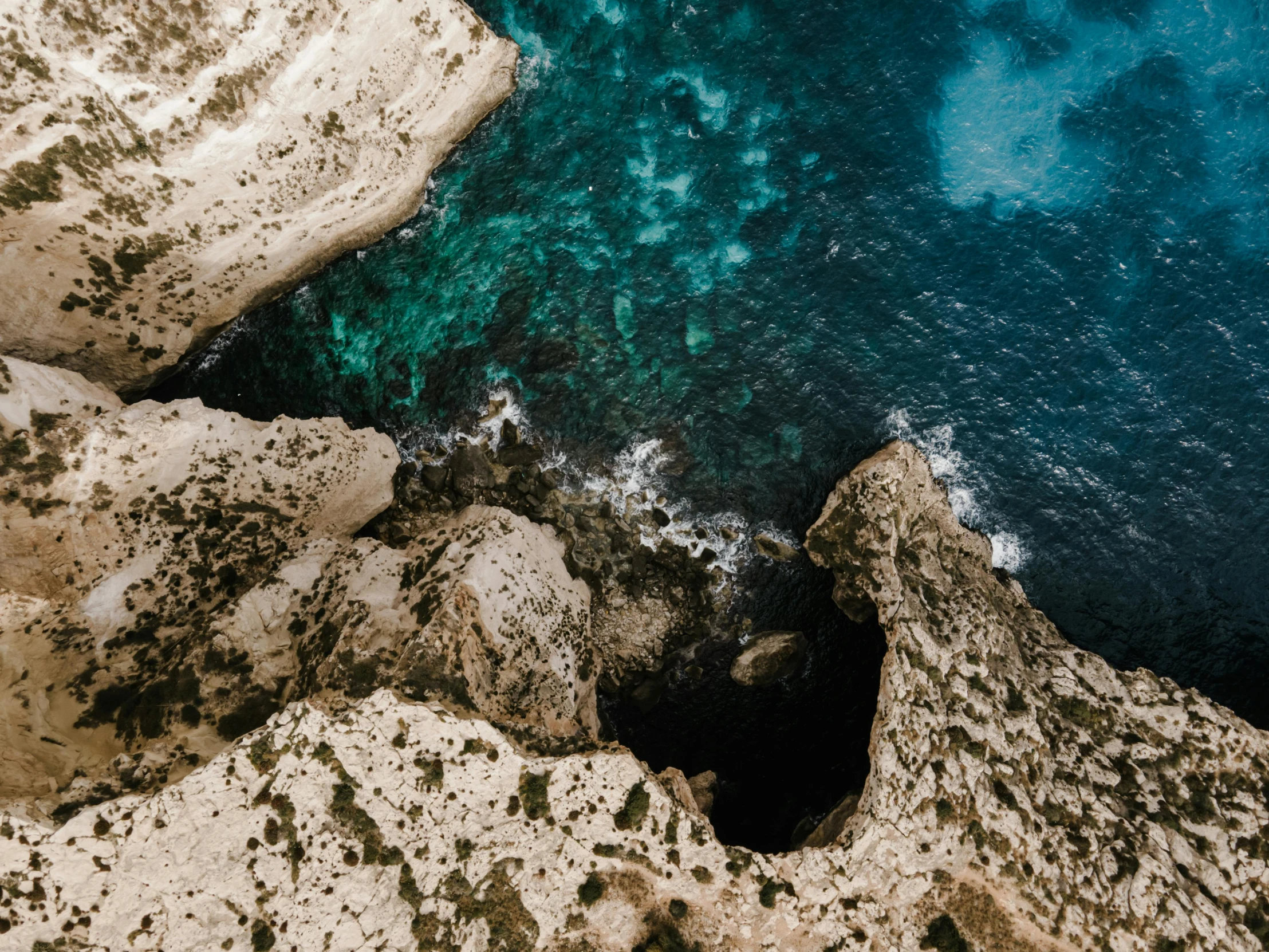 a man standing on top of a cliff next to the ocean, pexels contest winner, natural cave wall, close-up from above, teal aesthetic, black