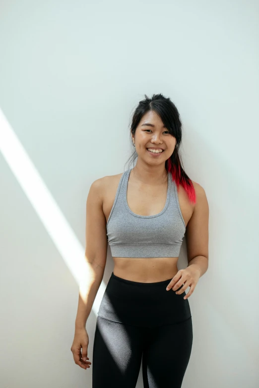 a woman standing in front of a white wall, inspired by helen huang, pexels contest winner, happening, detailed sports bra, smiling into the camera, indoor picture, croptop