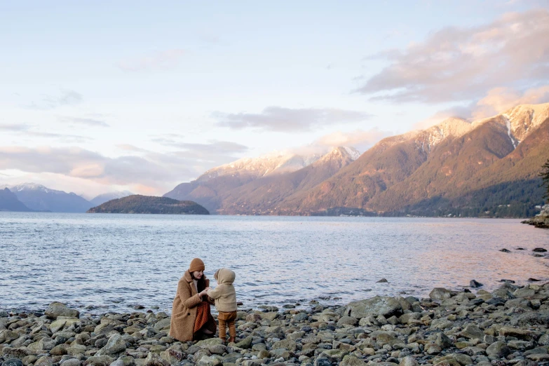 a couple of people sitting on top of a rocky beach, inspired by Steve McCurry, unsplash, lakeside mountains, wearing brown robes, new zealand, with a kid