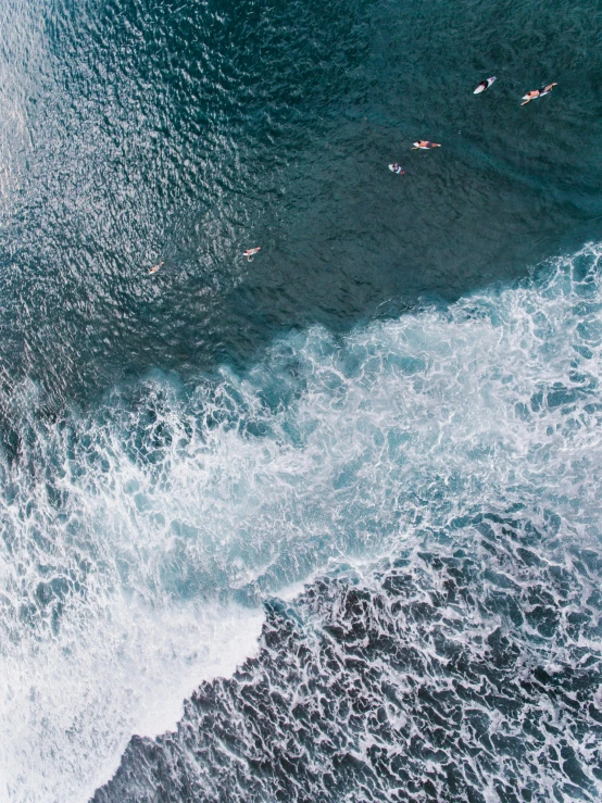 a group of people riding surfboards on top of a wave, helicopter view, black sand, clear blue water, unsplash 4k