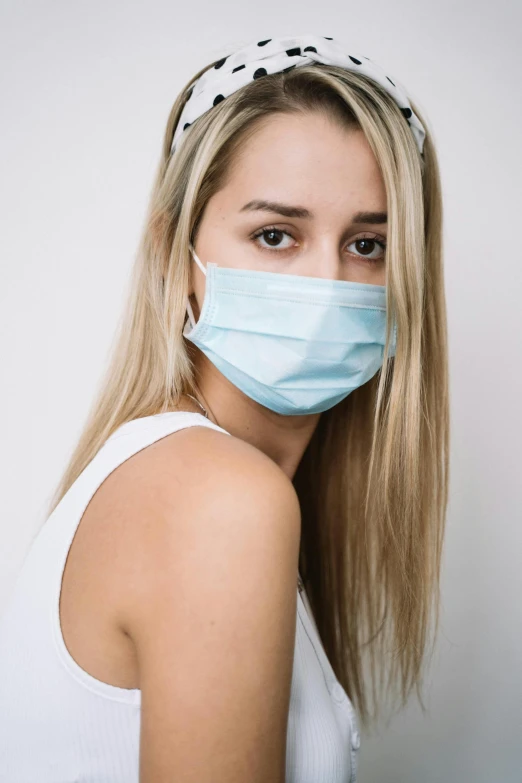 a woman wearing a face mask in front of a white wall, by Dan Luvisi, surgical supplies, close up of a blonde woman, light blue skin, handsome girl