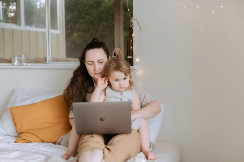 a woman sitting on top of a bed holding a baby, pexels, computer art, typing on laptop, brown, super focused, medium shot of two characters