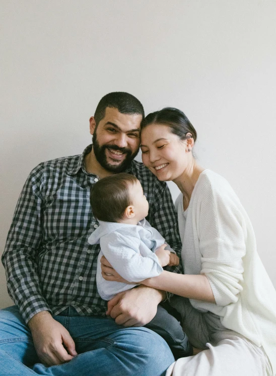 a man and woman sitting on a bed with a baby, a picture, pexels, with a small beard, promotional image, happy kid, mixed race