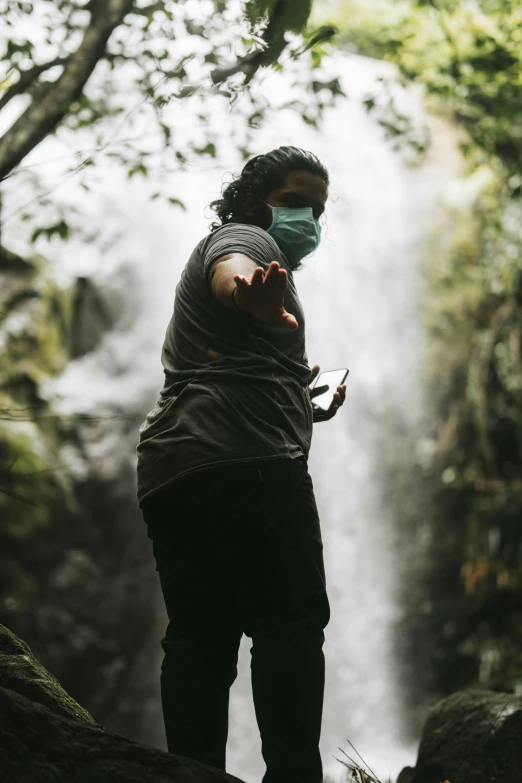 a woman wearing a face mask standing in front of a waterfall, sri lanka, mana shooting from his hands, concerned, slide show