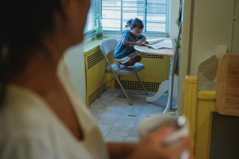 a woman sitting at a table in front of a window, a child's drawing, by Pablo Carpio, pexels contest winner, film still of manny pacquiao, healthcare worker, sitting in his highchair, high angle shot