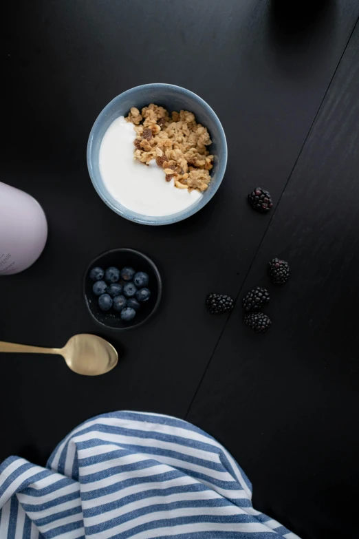 a black table topped with bowls of cereal and blueberries, minimalism, product image, subtle purple accents, yogurt, dwell