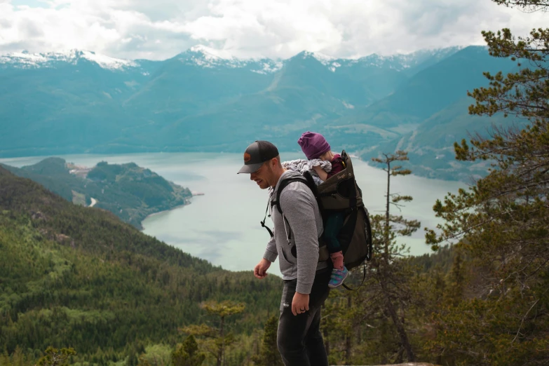 a man carrying a child on top of a mountain, pexels contest winner, vancouver, avatar image, parks and lakes, carrying a saddle bag