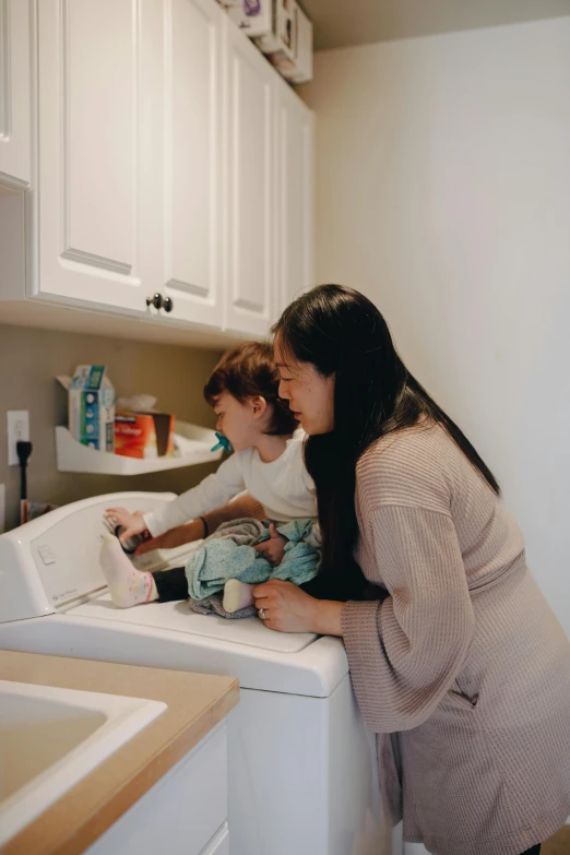 a woman standing next to a child in a kitchen, in a laundry mat, profile image, janice sung, families playing