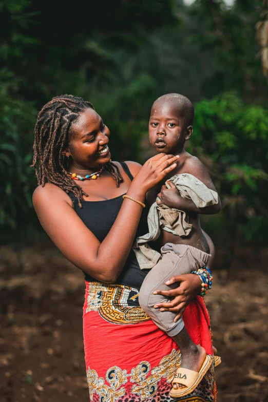 a woman holding a child in a forest, happening, intricate african jewellery, confident looking, item, information